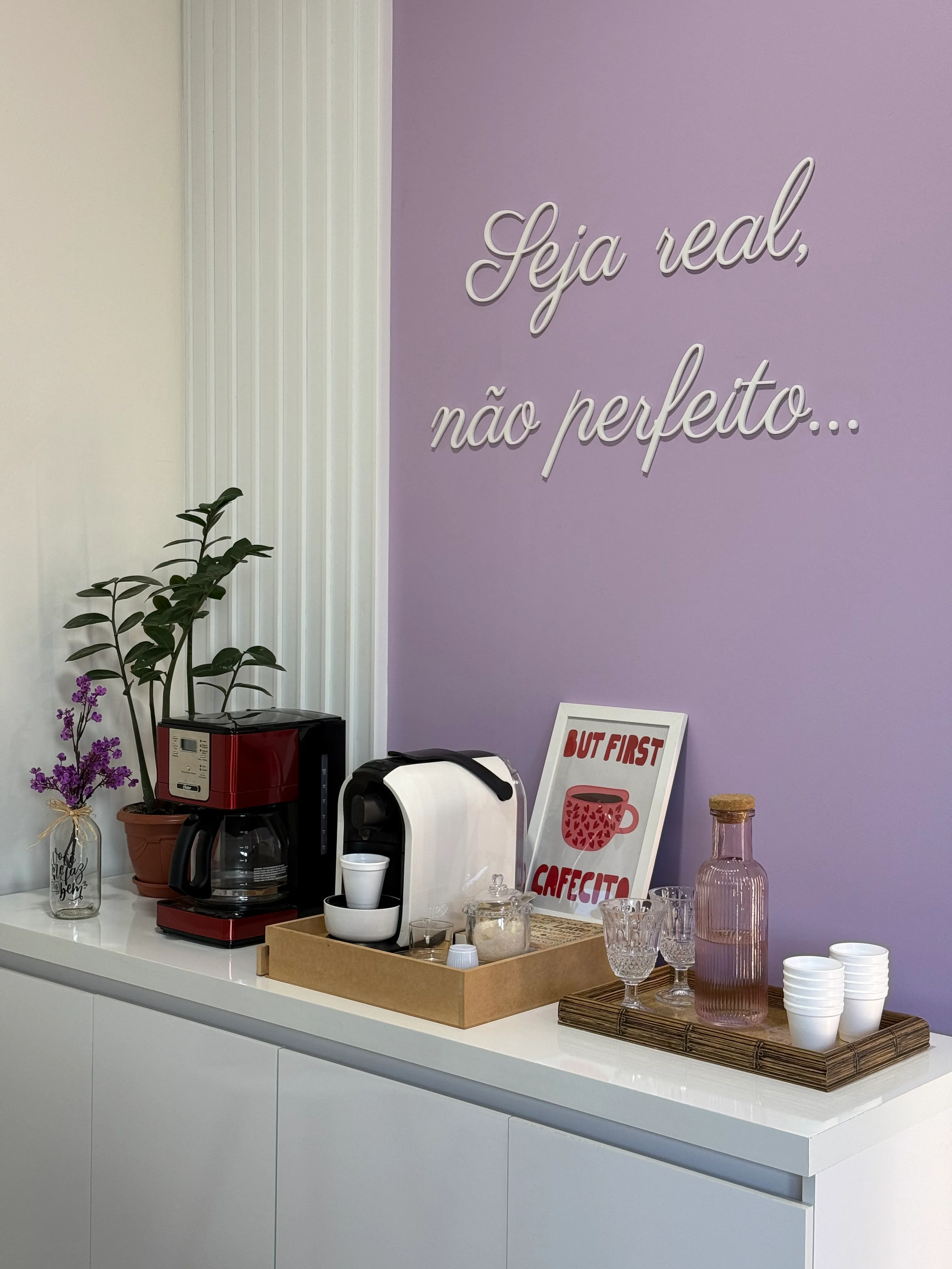 Detalhe da frase Seja real, não perfeito aplicada em letras brancas sobre a parede lilás